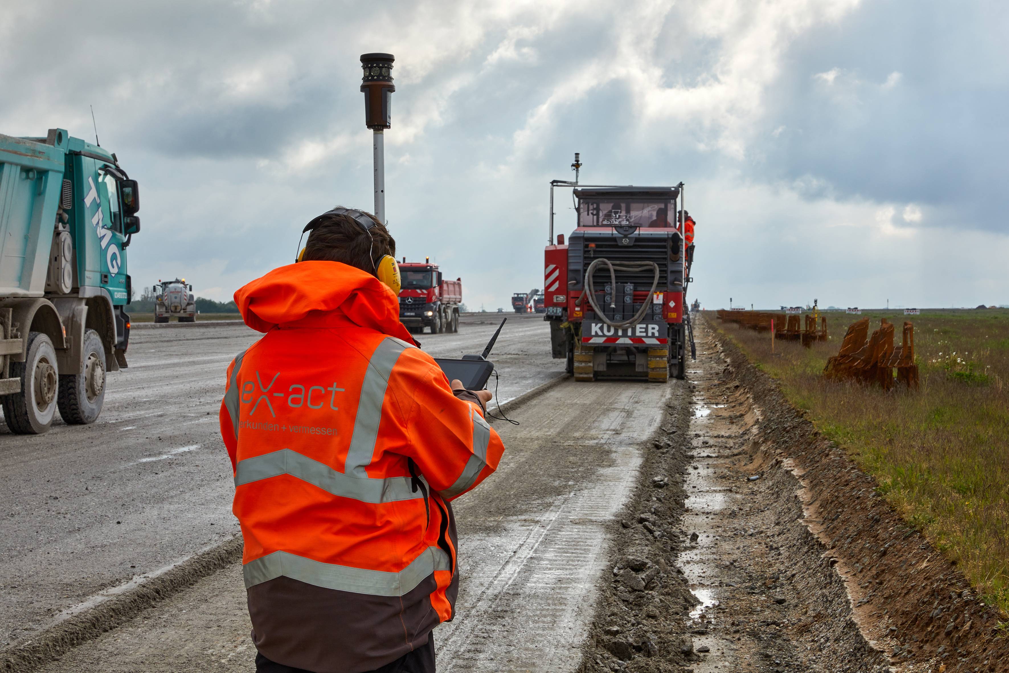 Operador com colete refletor monitora o trabalho de uma fresadora Wirtgen em funcionamento com o Sistema de Guia Trimble Roadworks 3