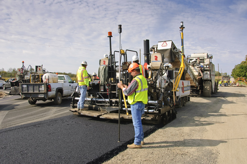 Operarios trabajando con una extendedora de asfalto equipada con sistemas de guiado avanzados que aseguran la precisión en el pavimentado