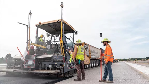 Trabalhadores com coletes refletores a operar uma pavimentadora de asfalto guiados pelo sistema Trimble Roadworks 3D