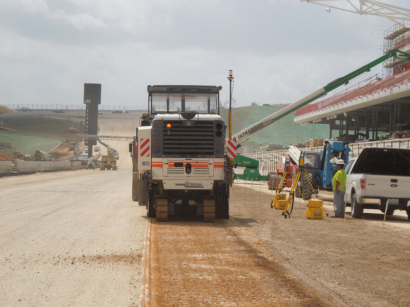 Máquina extendedora de asfalto Dynapac trabajando en un sitio de construcción con diversos equipos y trabajadores activos– ilustrando los sistemas de guiado para extendedoras y fresadoras de SITECH