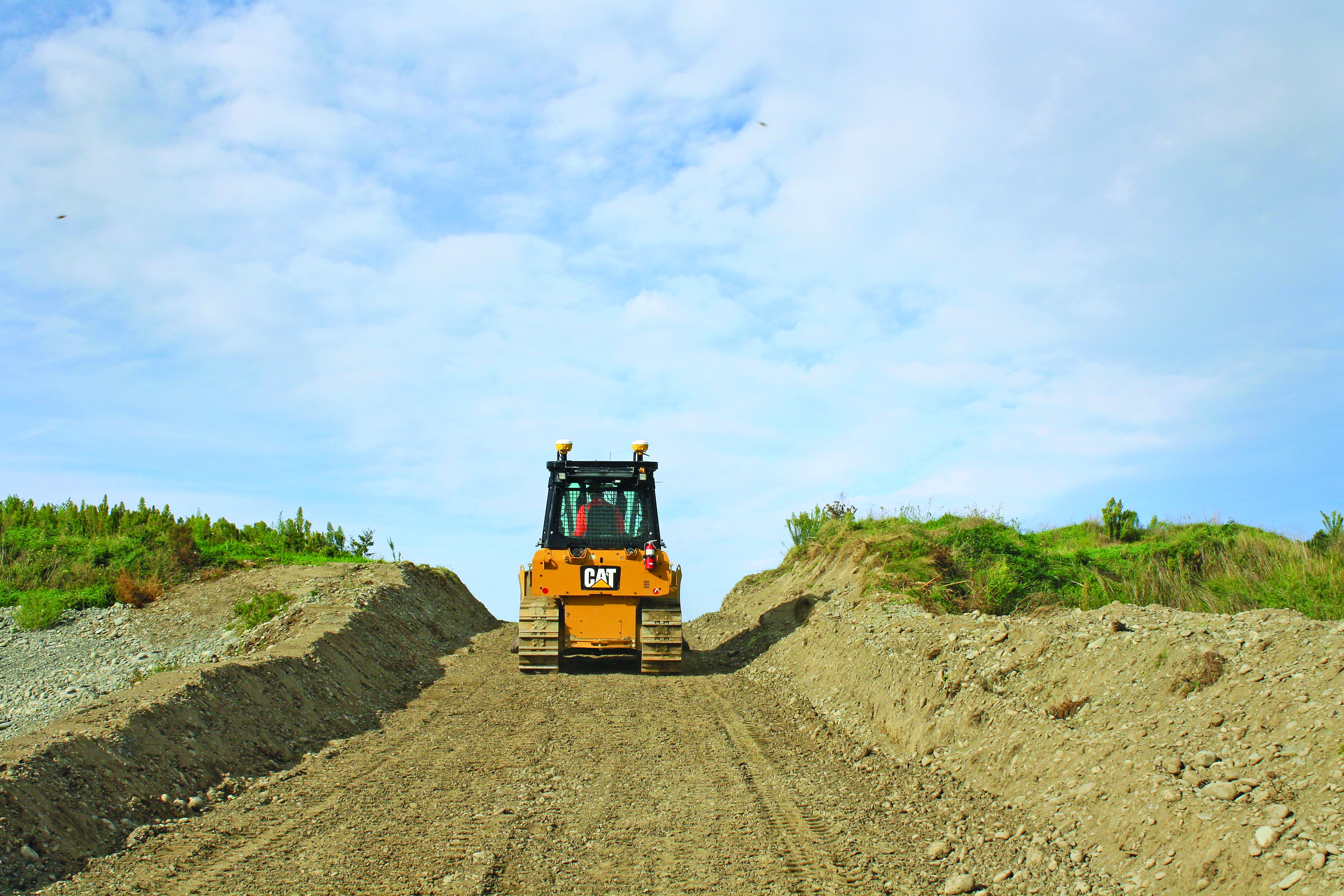 Um bulldozer CAT amarelo equipado com o sistema 3D Trimble Earthworks a trabalhar num terreno de construção com montes de terra em ambos os lados